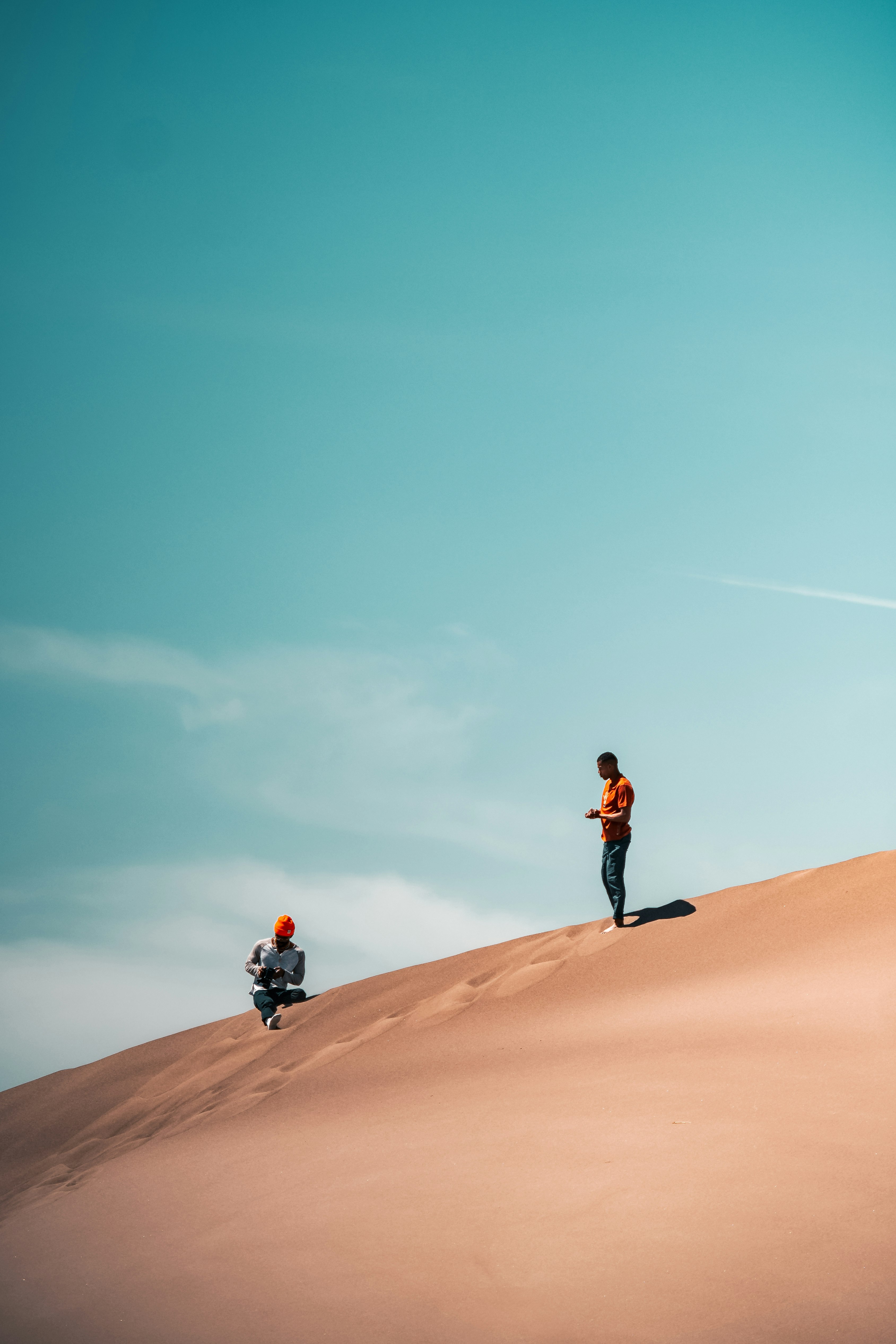 man in black jacket and black pants walking on brown sand under blue sky during daytime